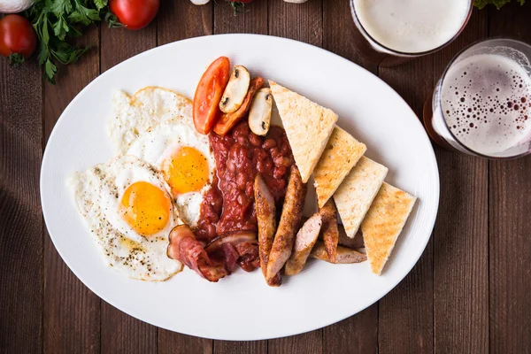 英式早餐（煎蛋、豆类、烤培根、香肠和蔬菜）在深色木材背景顶视图 — 图库照片