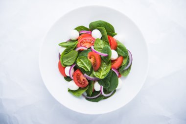 Beyaz arka plan üst görünümünde mozzarella peyniri, domates, ıspanak ve mor soğan ile taze salata