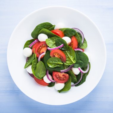 Mozzarella peyniri, domates, ıspanak ve mor soğan ile taze salata mavi ahşap arka plan üst görünümü