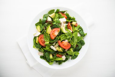 Beyaz ahşap arka plan üst görünümünde tavuk, domates, ıspanak ve avokado ile taze salata