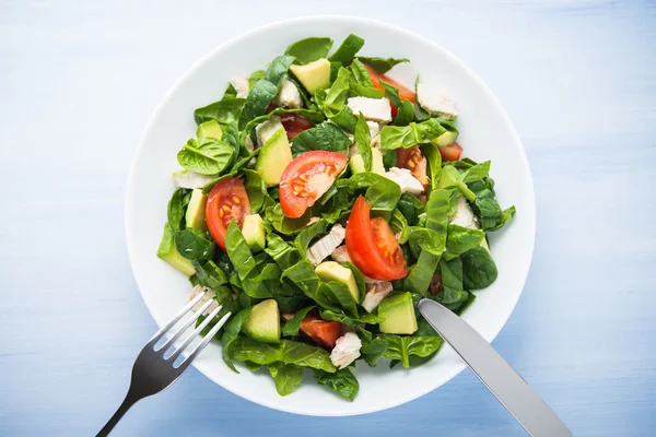 Frischer gesunder Salat mit Hühnchen, Tomaten, Spinat und Avocado auf blauem Holzhintergrund — Stockfoto