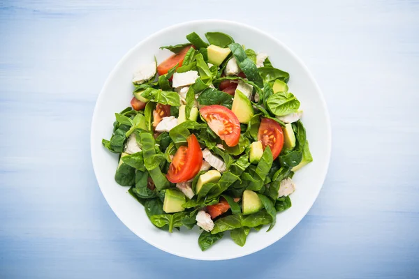 Frischer gesunder Salat mit Hühnchen, Tomaten, Spinat und Avocado auf blauem Holzhintergrund — Stockfoto