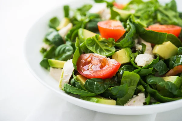 Ensalada fresca con pollo, tomates, espinacas y aguacate sobre fondo de madera blanca de cerca . — Foto de Stock