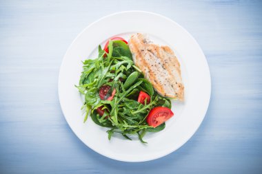 Kavrulmuş tavuk göğsü ve domates ve yeşillik (ıspanak, arugula) mavi ahşap arka plan üzerinde üst görünümü ile taze salata