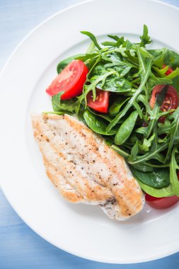 Kavrulmuş tavuk göğsü ve domates ve yeşillik (ıspanak, arugula) mavi ahşap arka plan üzerinde üst görünümü ile taze salata