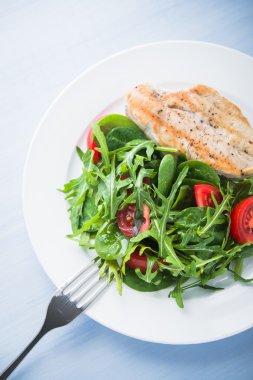 Kavrulmuş tavuk göğsü ve domates ve yeşillik (ıspanak, arugula) mavi ahşap arka plan üzerinde üst görünümü ile taze salata