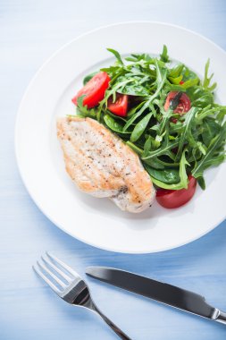 Kavrulmuş tavuk göğsü ve domates ve yeşillik (ıspanak, arugula) mavi ahşap arka plan üzerinde üst görünümü ile taze salata