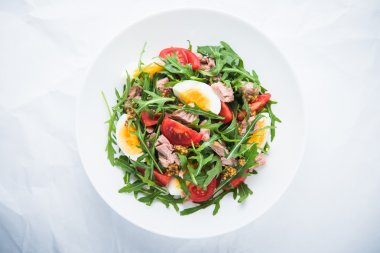 Ton balığı, domates, yumurta, arugula ve hardal ile taze salata beyaz dokulu arka plan üst görünümünde