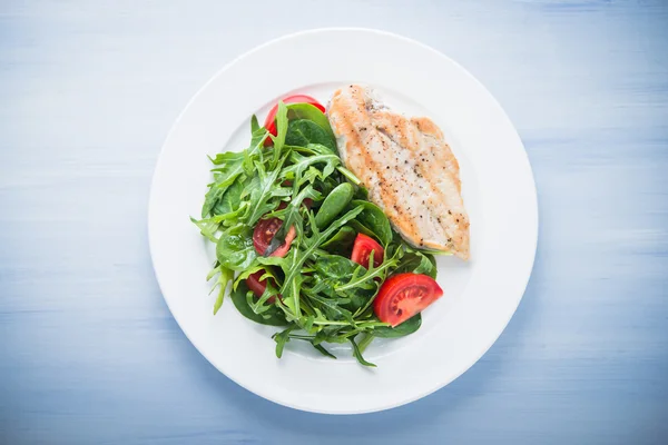 Peito de frango assado e salada fresca com tomate e verduras (espinafre, rúcula) vista superior sobre fundo de madeira azul — Fotografia de Stock