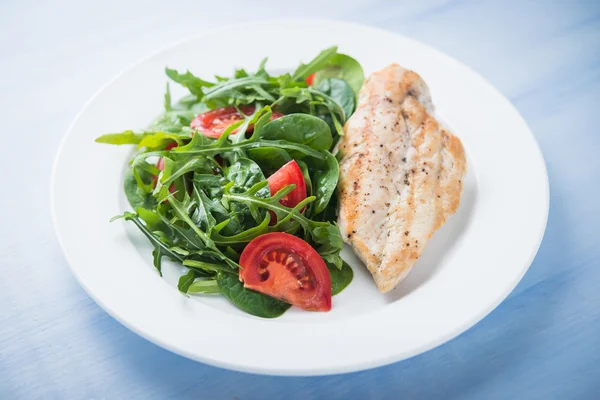 Gebratene Hühnerbrust und frischer Salat mit Tomaten und Gemüse (Spinat, Rucola) in Großaufnahme auf blauem Holzgrund — Stockfoto