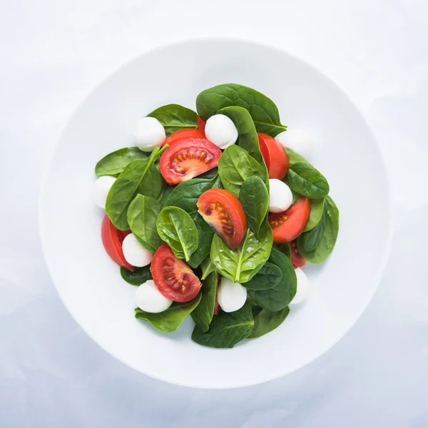 Fresh salad with mozzarella cheese, tomato and spinach on white paper background top view — Stock Photo, Image