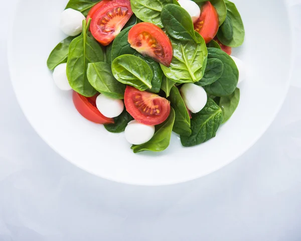 Frischer Salat mit Mozzarella, Tomate und Spinat auf weißem Papier Hintergrundbild von oben — Stockfoto