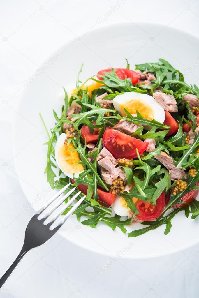 Fresh salad with tuna, tomatoes, eggs, arugula and mustard on white textured background top view