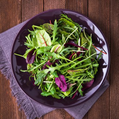 Koyu ahşap arka plan üst görünümünde karışık yeşillik (arugula, mesclun, pala) ile taze salata.