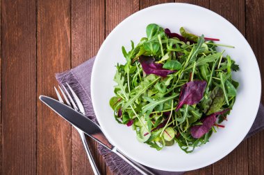 Koyu ahşap arka plan üst görünümünde karışık yeşillik (arugula, mesclun, pala) ile taze salata.
