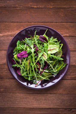 Koyu ahşap arka plan üst görünümünde karışık yeşillik (arugula, mesclun, pala) ile taze salata.