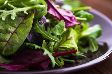 Koyu ahşap arka plan üzerinde karışık yeşillik (arugula, mesclun, pala) ile taze salata yakın.