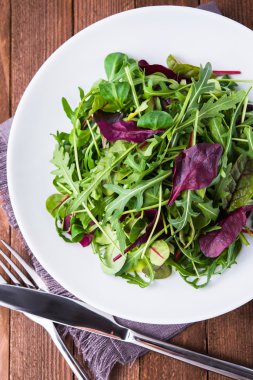 Koyu ahşap arka plan üst görünümünde karışık yeşillik (arugula, mesclun, pala) ile taze salata.