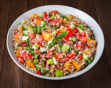 Quinoa ile taze sağlıklı salata, renkli domates, tatlı biber, salatalık ve maydanoz ahşap arka plan yakın.