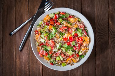 Ahşap arka plan üst görünümünde Quinoa, renkli domates, tatlı biber, salatalık ve maydanoz ile taze sağlıklı salata.