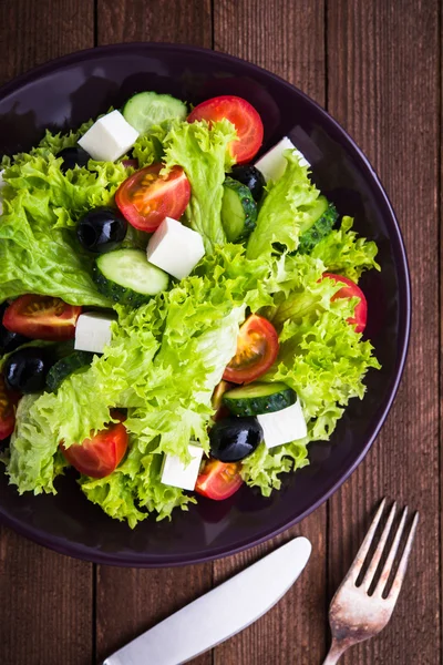 Salată grecească (salată verde, roșii, brânză feta, castraveți, măsline negre) pe fundal întunecat din lemn vedere de sus . — Fotografie, imagine de stoc