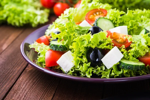 Salada grega (alface, tomate, queijo feta, pepino, azeitonas pretas) em fundo de madeira escura close up . — Fotografia de Stock