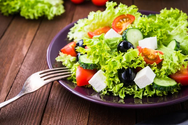 Griechischer Salat (Salat, Tomaten, Feta-Käse, Gurken, schwarze Oliven) auf dunklem Holzgrund in Nahaufnahme. — Stockfoto