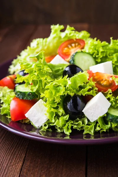 Görög saláta (fejes saláta, paradicsom, feta sajt, uborka, fekete olajbogyó), sötét fából készült háttér közelről. — Stock Fotó