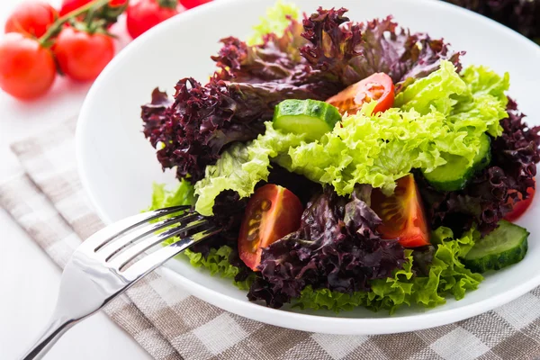 Salada fresca com alface verde e roxa, tomates e pepinos em fundo de madeira branca close up . — Fotografia de Stock