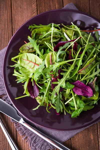 Salada fresca com verduras mistas (arugula, mesclun, mache) em fundo de madeira escura vista superior . — Fotografia de Stock