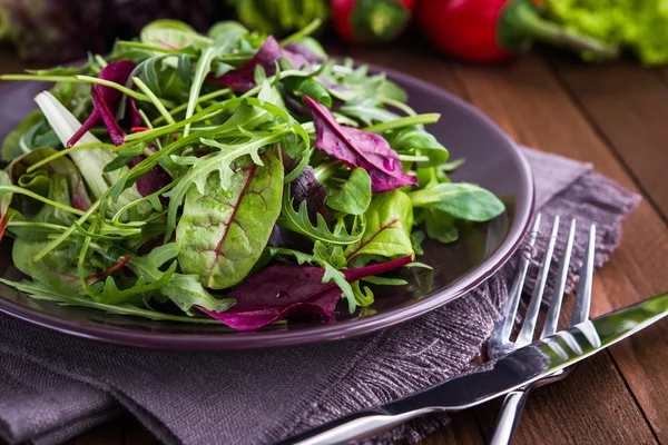 Salade fraîche aux légumes verts mélangés (roquette, mesclun, mache) sur fond bois foncé gros plan . — Photo