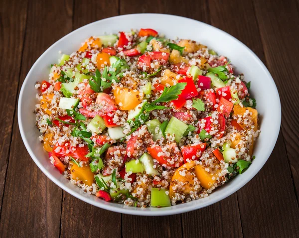 Verse gezonde salade met quinoa, kleurrijke tomaten, paprika, komkommer en peterselie op houten achtergrond close-up. — Stockfoto