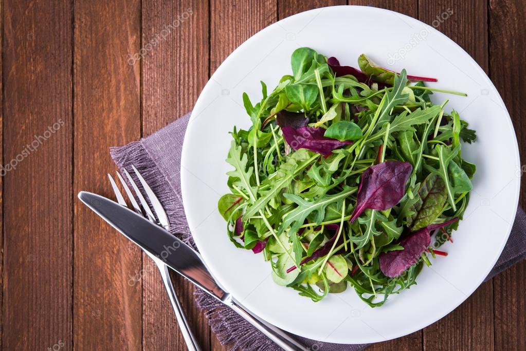 Fresh salad with mixed greens (arugula, mesclun, mache) on dark wooden background top view.