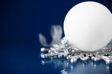 White and silver christmas ornaments on dark blue background with space for text.