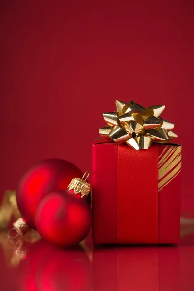 Red gift box with golden ribbons and xmas baubles on red background. — Stock Photo, Image