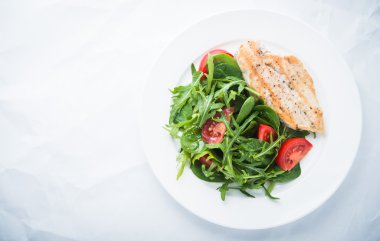 Kavrulmuş tavuk göğsü ve domates ve yeşillik (ıspanak, arugula) beyaz dokulu arka plan üst görünümü ile taze salata.