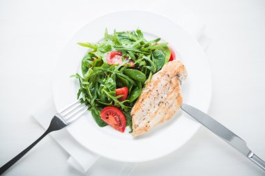 Tavuk göğsü ve domates ve yeşillik (ıspanak, arugula) beyaz ahşap arka plan üzerinde üst görünümü ile taze salata.