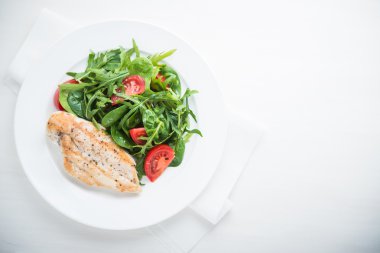 Kavrulmuş tavuk göğsü ve domates ve yeşillik (ıspanak, arugula) beyaz ahşap arka plan üzerinde üst görünümü ile taze salata.