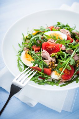 Ton balığı, domates, yumurta, roka ve mavi ahşap zemin üzerine hardal ile taze salata yakın çekim.