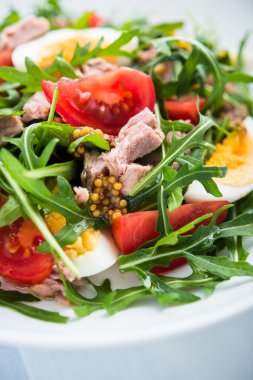 Ton balığı, domates, yumurta, roka ve mavi ahşap zemin üzerine hardal ile taze salata yakın çekim.