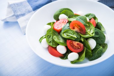 Mozzarella peyniri, domates, ıspanak mavi ahşap zemin üzerine taze salata yakın çekim.