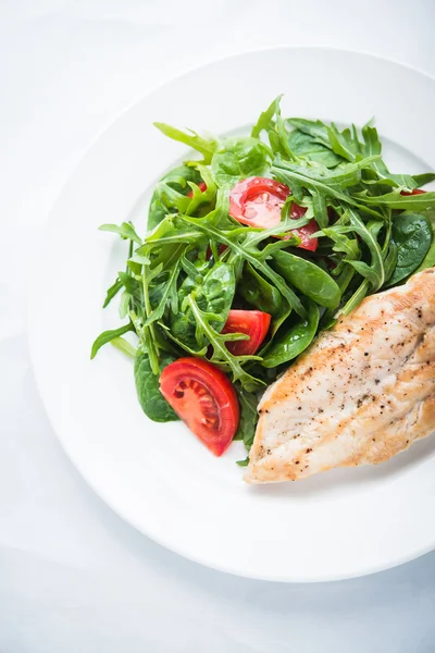 Tavuk göğsü ve domates ve yeşillik (ıspanak, arugula) beyaz ahşap arka plan üzerinde üst görünümü ile taze salata.