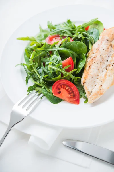 Kavrulmuş tavuk göğsü ve domates ve yeşillik (ıspanak, arugula) ile taze salata beyaz ahşap arka plan üzerinde yakın.
