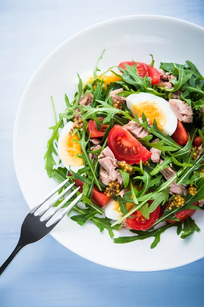 Ton balığı, domates, yumurta, arugula ve hardal ile taze salata mavi ahşap arka plan üst görünümünde.