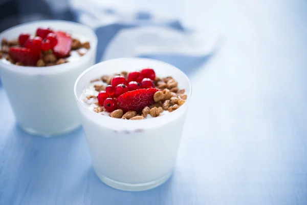 Iogurte com cereais e bagas em fundo azul (café da manhã saudável ) — Fotografia de Stock