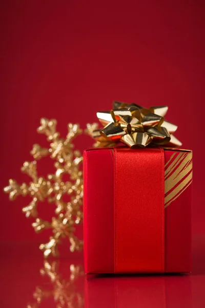 Kırmızı hediye kutusu ve xmas kar tanesi kırmızı zemin üzerine. Mutlu Noeller. — Stok fotoğraf