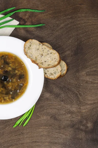 Lenten quadragesimal vegetarian soup with wild mushrooms, pearl barley, fresh herbs and healthy cereal bread. Traditional dish in a white plate on a wooden background, top view, vertical, copy space — Stock Image Lenten Quadragesimal Vegetarian Soup Wild Mushrooms Pearl Barley Fresh Herbs Stock Image