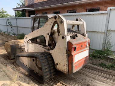 Geniş kovalı küçük bir traktör. Küçük inşaat malzemeleri. Sürüngen kazıcı zemini düzleştiriyor. Irpin, Kiev bölgesi, 10 Ekim 2020