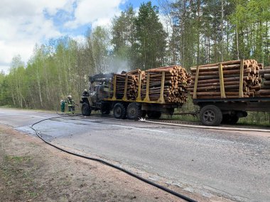 İtfaiyeciler ormanın yakınındaki bir kamyonu söndürüyor. Duman ve yangın kamyonun taksisinde. Odun taşıyıcı yangından dolayı duman içinde. Radomyshl Köyü, Zhytomyr bölgesi, Ukrayna 4 Mayıs 2021