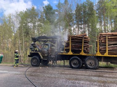 İtfaiyeciler ormanın yakınındaki bir kamyonu söndürüyor. Duman ve yangın kamyonun taksisinde. Odun taşıyıcı yangından dolayı duman içinde. Radomyshl Köyü, Zhytomyr bölgesi, Ukrayna 4 Mayıs 2021